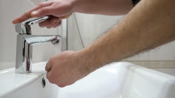 Middle-aged man washes his hands under a stainless steel faucet in slow motion                                A exciting closeup of a stainless steel fauced opened by a middle-aged man in a bathroom. He washes his hands under the streem in slo-mo - Video, Çekim