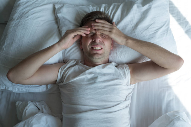 mies makaa kotona sängyssä ja kärsii päänsärystä tai krapulasta
 - Valokuva, kuva
