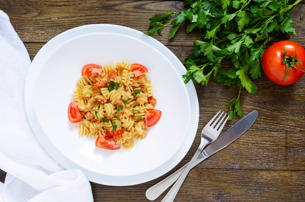 Warm salad with seafood in a white bowl on a wooden background. Pasta Radiatori with crayfish, shrimp, tomatoes, herbs and creamy garlic sauce. - Foto, Imagen