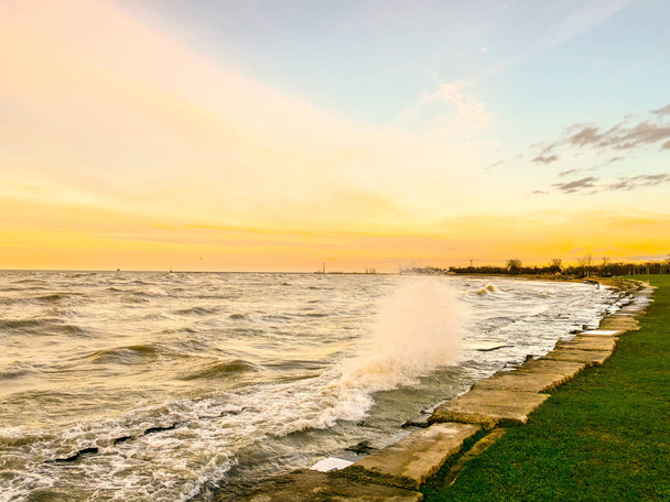 大きな波クラッシュに対してコンクリートの階段状の海岸線とシカゴの地平線のかなたのオレンジと青の空が夕日であるミシガン湖沿いの美しい風景写真. - 写真・画像