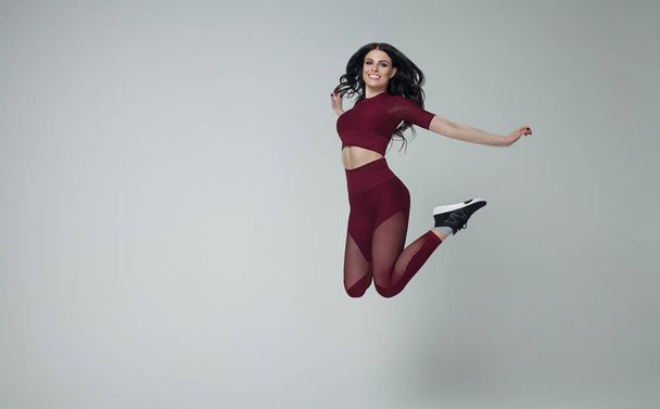 Portrait of fit and sporty young woman jumping on grey background. - Zdjęcie, obraz