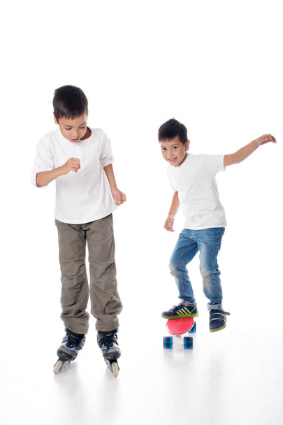 Deux garçons roulent des patins à roulettes et une planche sur fond blanc en studio
 - Photo, image
