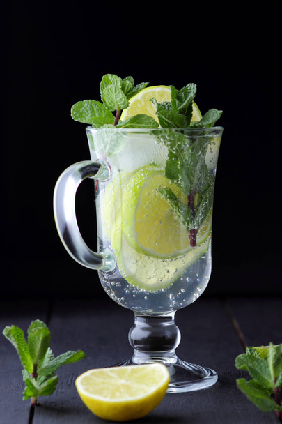 Mojito on a dark background, summer cocktail with lime, refreshing drink with lemon, fresh mint for cocktail, celebratory drink with ice, vegan, copy space, minimalist cocktail - Foto, afbeelding
