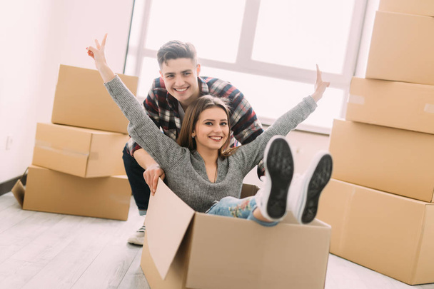 Happy young smile couple is having fun with cardboard boxes in new house at moving day. - 写真・画像