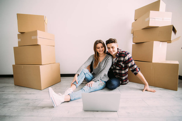 Young couple moving in new home sitting on floor and relaxing after unpacking looking something on laptop. Relocation - Φωτογραφία, εικόνα