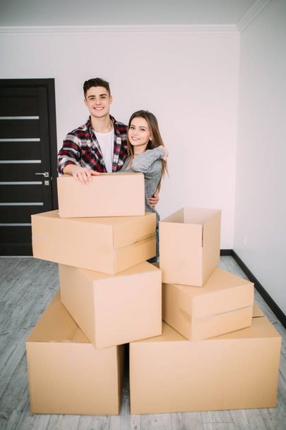Usmívající se pár opírající se o boxy v novém domově. Mladý pár přestěhoval do nového bytu společně přemístění - Fotografie, Obrázek