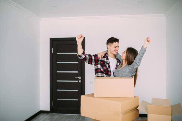 cheerful and happy young couple victory raised hands of their new home with moving cardboard box during move into new apartment - Photo, Image
