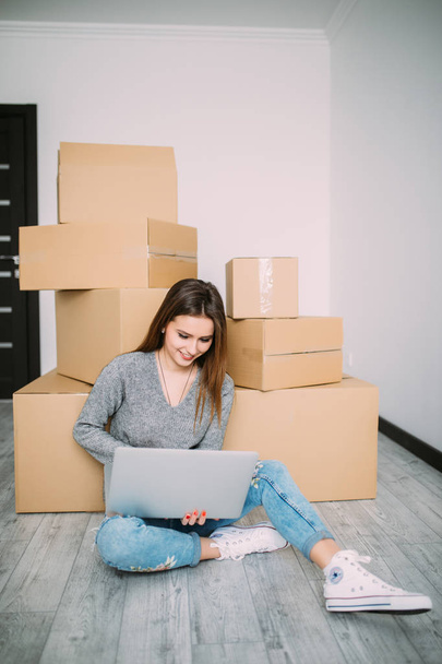 Młoda kobieta, poruszające się w nowe mieszkanie, siedząc na podłodze i przeglądania Internetu na laptopie w poszukiwaniu nowych pomysłów dekoracji. - Zdjęcie, obraz