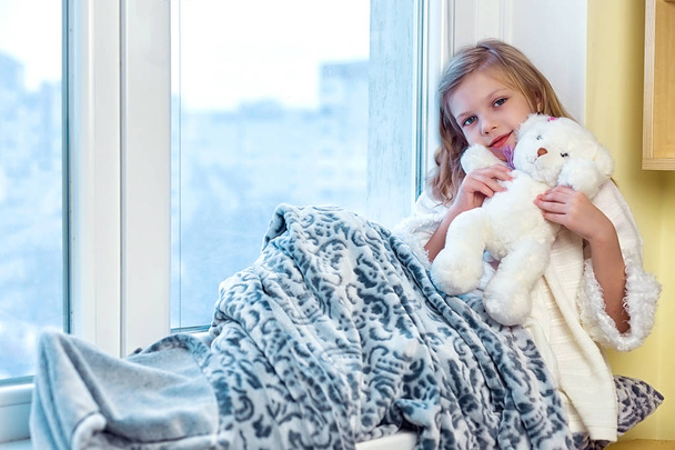 かわいい女の子がテディベアを抱いてします。冬に窓際に座っているかわいい赤ちゃんの部屋 - 写真・画像