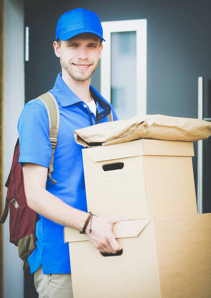 Hymyilevä postimies sinisessä univormussa toimittamassa pakettilaatikkoa vastaanottajalle kuriiripalvelun konsepti. Hymyilevä lähetti sinisessä univormussa. - Valokuva, kuva