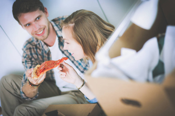 Young couple have a pizza lunch break on the floor after moving into a new home with boxes around them. Young couple - Fotografie, Obrázek