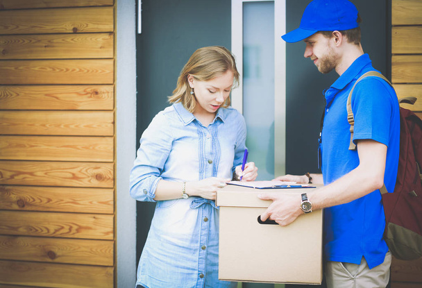 Smiling delivery man in blue uniform delivering parcel box to recipient - courier service concept. Smiling delivery man in blue uniform - Foto, Imagen