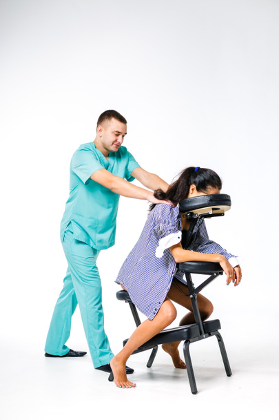 Tema masaje y oficina. Terapeuta masculino con traje azul haciendo masaje de espalda y cuello para trabajadora joven, mujer de negocios con camisa en silla de masaje shiatsu
 - Foto, Imagen