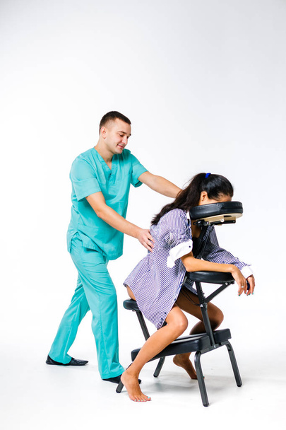Thema Massage und Büro. männlicher Therapeut mit blauem Anzug bei Rücken- und Nackenmassage für junge Arbeiterinnen, Geschäftsfrau im Hemd auf Massagestuhl Shiatsu - Foto, Bild