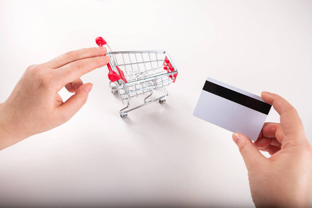 Bank card nearby a laptop and mini shopping cart on white background top view. - 写真・画像
