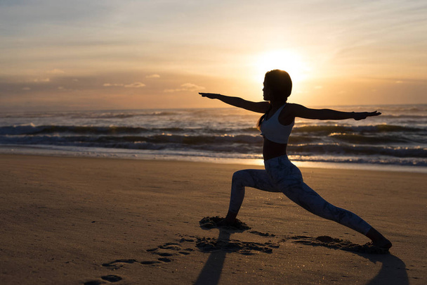 健康的な生活と精神的な開発と体の自然なバランスの概念をビーチでのヨガの練習を行うスポーティな若い女性のシルエット - 写真・画像