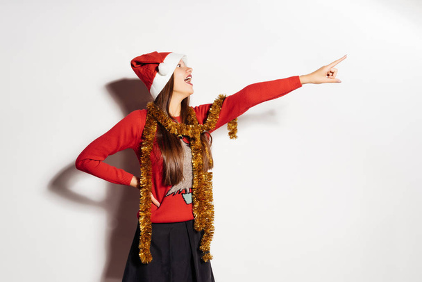happy girl in a red cap and a New Year's sweater shows something on - Foto, Imagen