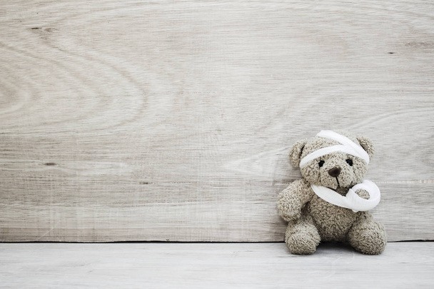 Teddybär mit Verbänden und gebrochener Hand auf Holz Hintergrund in, b - Foto, Bild