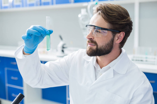 Kemiallinen koe Mukava positiivinen vakava mies yllään suojalasit ja pitämällä koeputki tehdessään kemiallisen kokeen
 - Valokuva, kuva