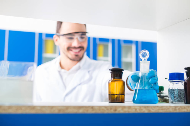 Lab inside. Selective focus of male hand taking lab glasses with liquids poured in and standing on surface - Photo, Image