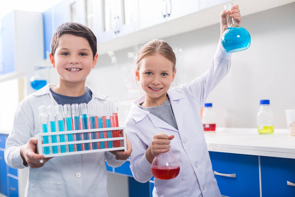 Chemistry lesson. Nice positive smart children looking at you and carrying chemical reagents while having a chemistry lesson - Foto, Imagem