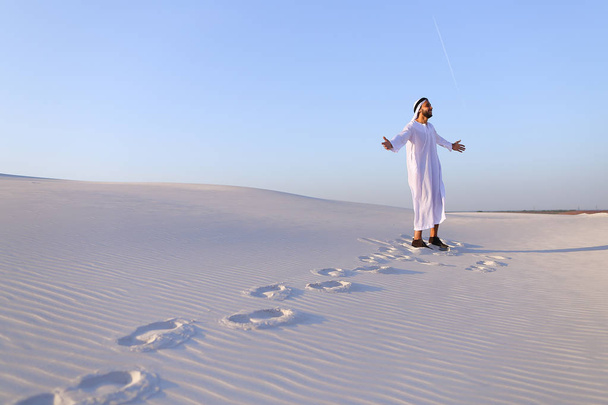 Joyful male Muslim walks through white sand desert and enjoys li - Photo, image
