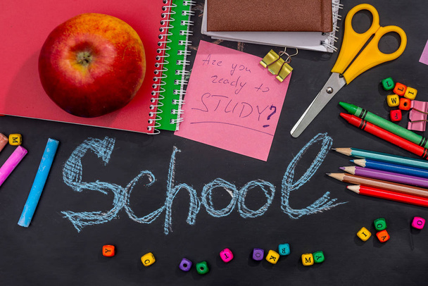 vele schoolbenodigdheden en appels op zwart blackboard - Foto, afbeelding