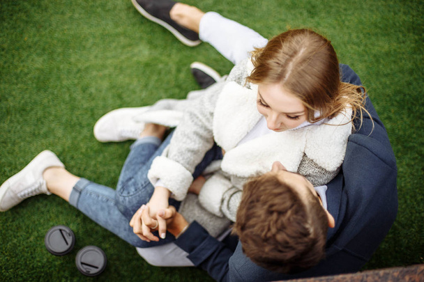 Young loving couple relaxing on grass and hugging, she is smiling and leaning on his shoulder, relationships and feelings concept - Foto, Imagen