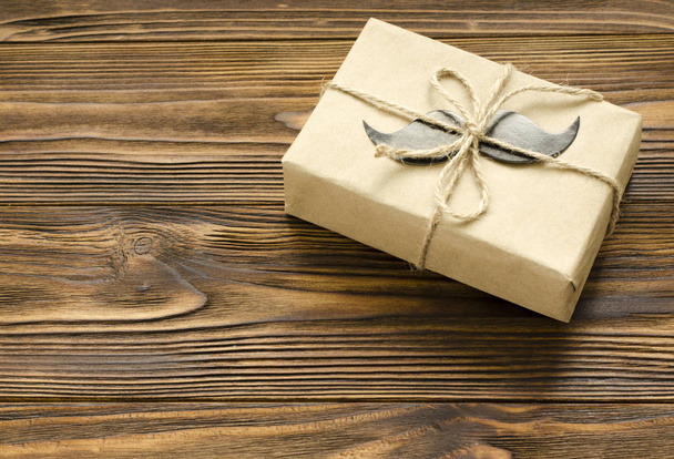 gift box wrapped in kraft paper with paper mustache on brown woo - Φωτογραφία, εικόνα
