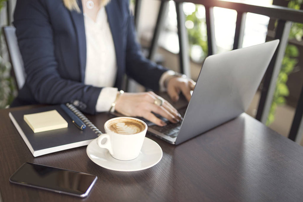 Business woman indoor with coffee and laptop on wooden table - Photo, image