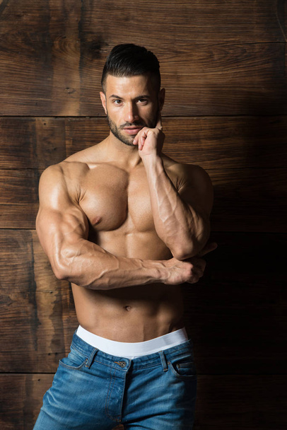 Model Flexing Muscles Against the Wooden Wall - Photo, Image