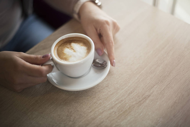 茶色の木製のテーブルの上のコーヒー カップを保持している女性の手 - 写真・画像