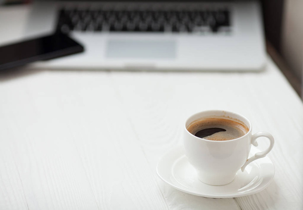 Kaffeetasse auf dem Holztisch auf verschwommenem Laptop-Hintergrund für Geschäftskonzept. - Foto, Bild