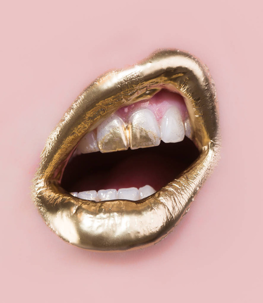 Golden lip tvoří. Zlatá barva na rty a zuby. Otevřená ústa a bílé zuby, které jsou izolovány na růžovém pozadí. Část bohatých obličeje pokryta zlatem. Moderní make-up pro ženy. Smyslné zlaté luxusní koncept - Fotografie, Obrázek
