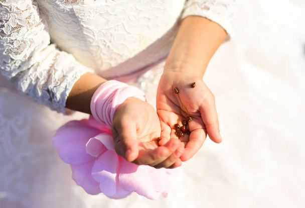Весна и девочка с жуками. Руки маленькой девочки в белом платье с розовым бантом. Ювелирные изделия и аксессуары, природа в городе, весеннее солнце. Красотка. Кожа на руках. Естественная косметика
 - Фото, изображение