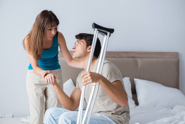 Young wife supporting husband on crutch after injury - Foto, afbeelding
