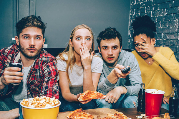 Close up of four people that look very scared and sad. They are watching scareful movie. Its veru interesting and terrible at the same time. They even has stopped eating food. - Foto, Imagem