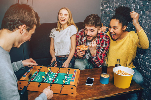 A shot where boys are playing football board game on the table while girls are cheering. Everybody is happy thinking only about the game. - Foto, imagen
