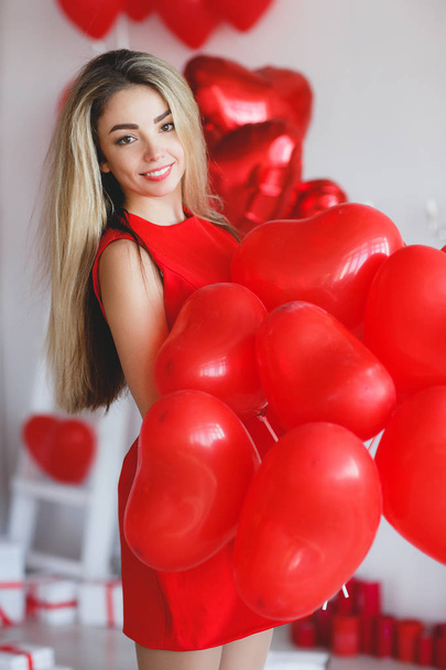 Beauty Valentine's Day Woman with red balloons. Fashion Model Girl face profile Portrait with red balloons in the shape of heart in her hand. Red Lips and Nails. Pink blurred background. Beautiful Luxury Makeup and Manicure, hair. - Foto, imagen