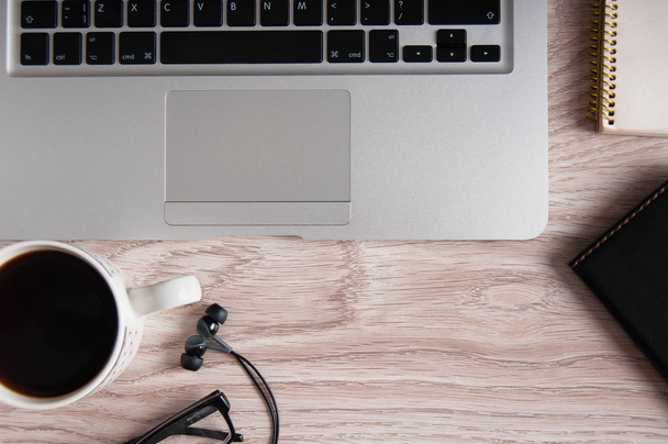 Vista dall'alto di laptop e blocco note con occhiali e cuffie sul desktop in legno e tazza di caffè
. - Foto, immagini