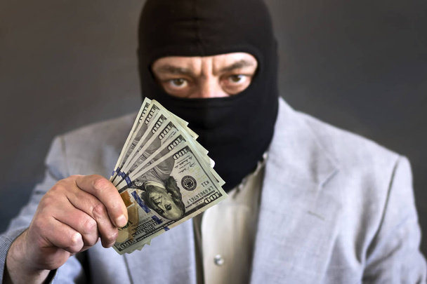 Businessman in balaclava with dololors in hands on dark background. Crime. Theft. - Photo, Image