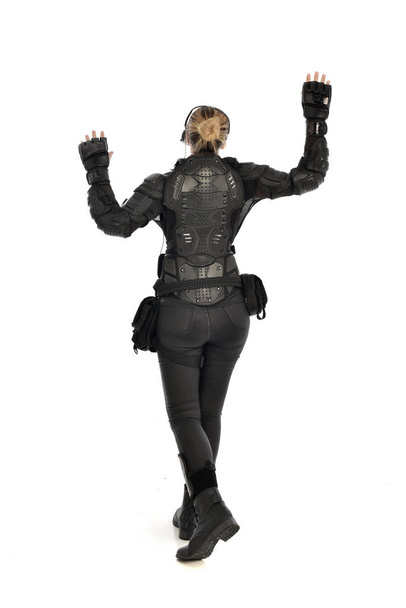 Ganzes Porträt einer Soldatin in schwarzer taktischer Rüstung, die sich von der Kamera abwendet, isoliert auf weißem Studiohintergrund. - Foto, Bild