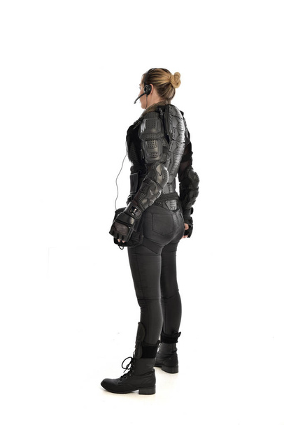 retrato de cuerpo entero de una soldado vestida con una armadura táctica negra frente a la cámara, aislada sobre fondo blanco del estudio
. - Foto, imagen