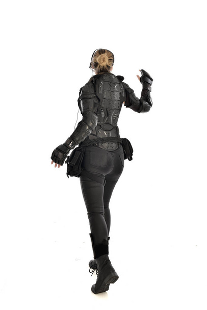 Ολόσωμο πορτρέτο του γυναίκα στρατιώτη που φορούσε μαύρο τακτικό πανοπλία που αντιμετωπίζει μακριά από την κάμερα, απομονώνονται σε φόντο λευκό στούντιο. - Φωτογραφία, εικόνα