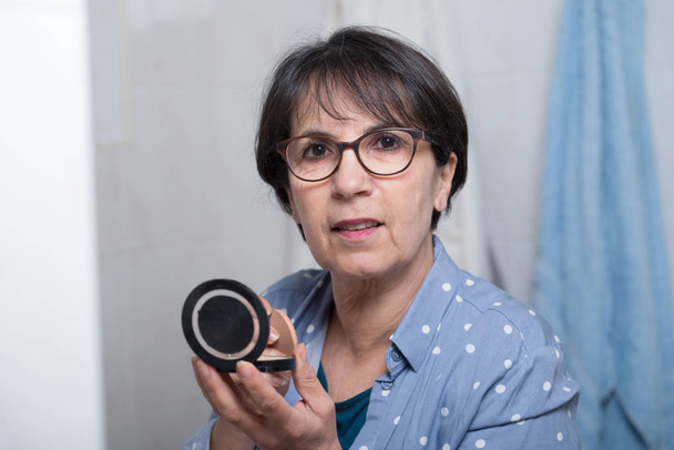 Starsza kobieta robi makijaż patrząc na małe lusterko - Zdjęcie, obraz