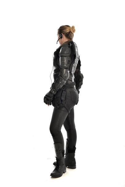 Pełna długość Portret żołnierz Kobieta w czarnej zbroi taktyczne stojące z dala od aparatu, na białym tle na tle białego studia. - Zdjęcie, obraz