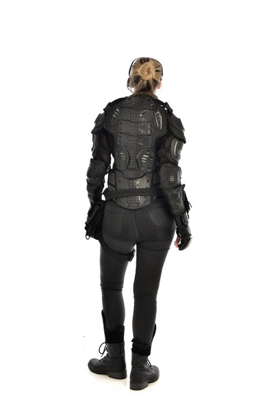 volledige lengte portret van vrouwelijke soldaat het dragen van zwarte tactische armour geconfronteerd weg van de camera, geïsoleerd op witte studio achtergrond. - Foto, afbeelding
