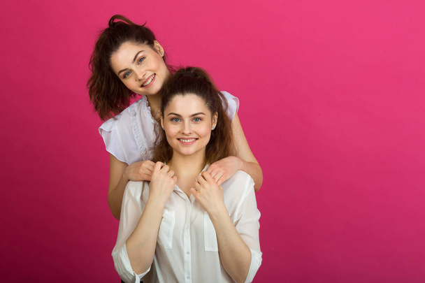 two beautiful young sisters twins in a good mood in white blouses on a pink background - Φωτογραφία, εικόνα