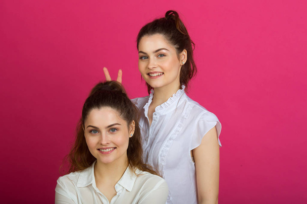 two beautiful young sisters twins in a good mood in white blouses on a pink background - Fotografie, Obrázek
