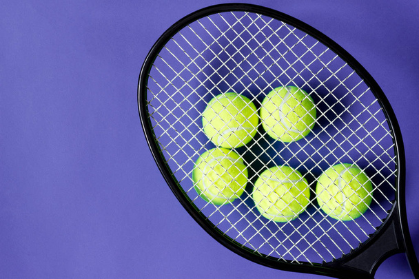 Siyah raketin altında tenis topları. Violet geçmişi. Spor kavramı. - Fotoğraf, Görsel